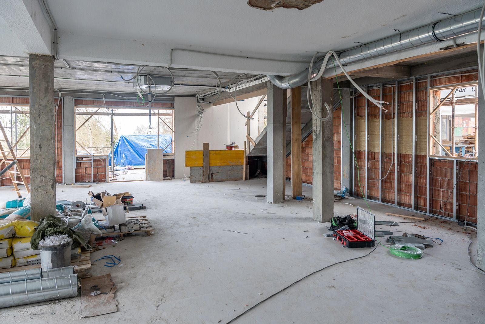 Unfinished interior with concrete columns, exposed wiring, and construction materials scattered on the floor.