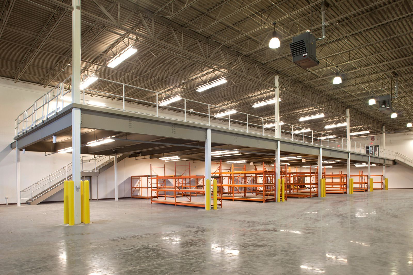 Empty warehouse interior with mezzanine stairs, orange shelving, and polished concrete floor