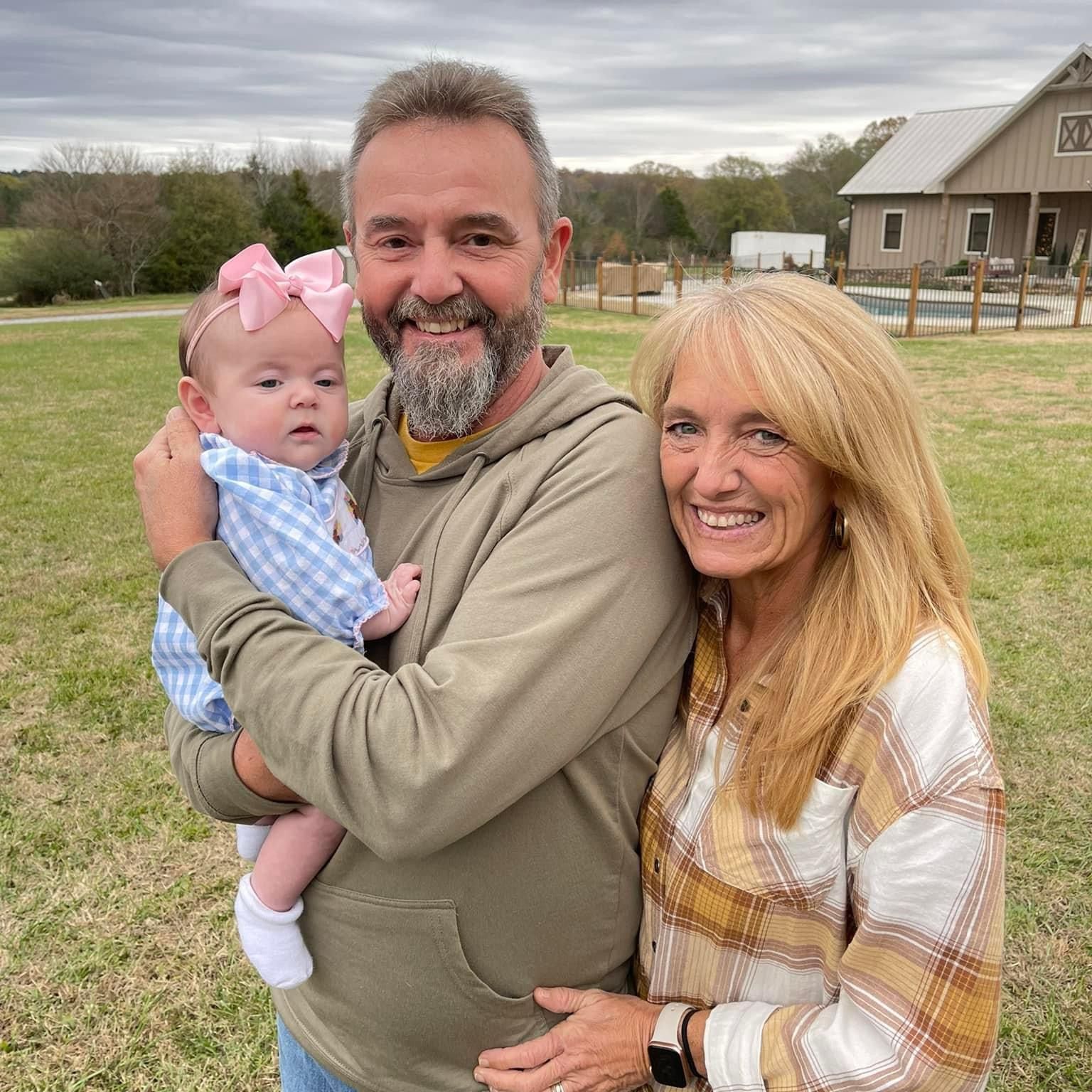 A man and woman are holding a baby in a field.