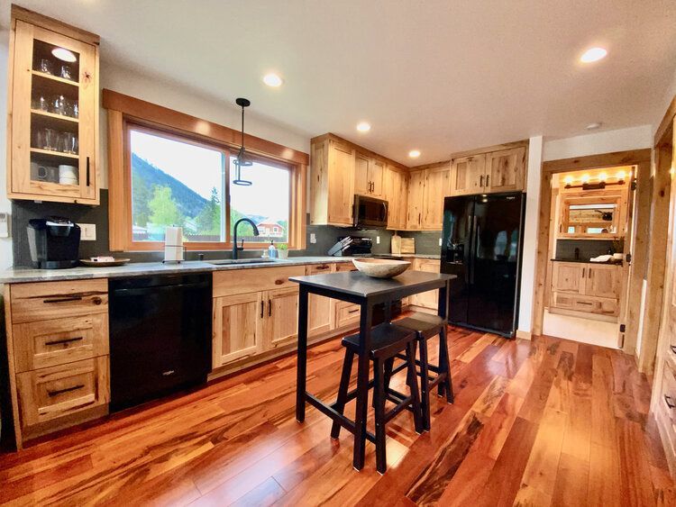 A kitchen with hardwood floors, wooden cabinets,  a refrigerator a sink, and a small island.