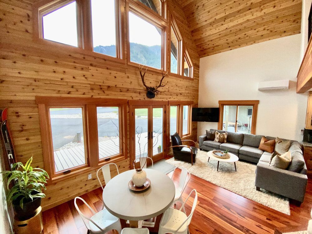 A overview of a living room with a couch, and a dining room  and  deer antlers on the wall.