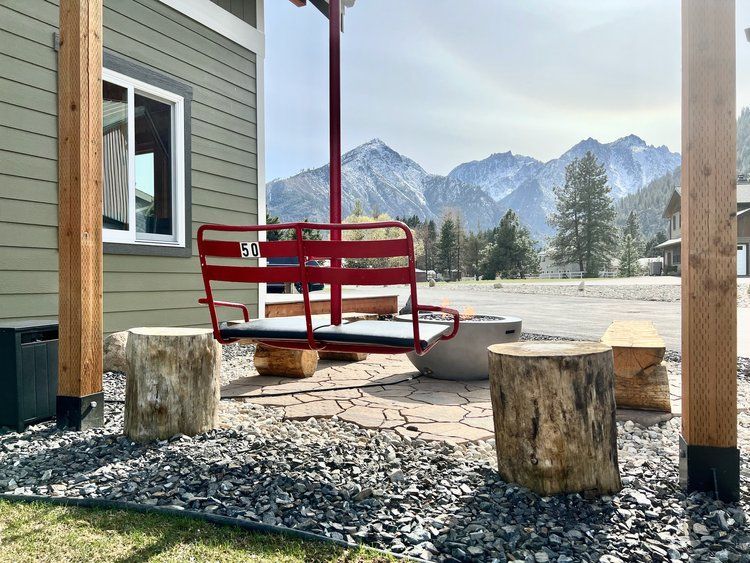 A red chairlift swing is sitting in front of a house with mountains in the background.