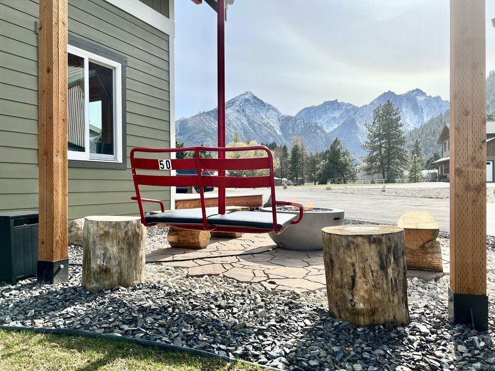 A red chairlift swing is sitting in front of a house with mountains in the background.