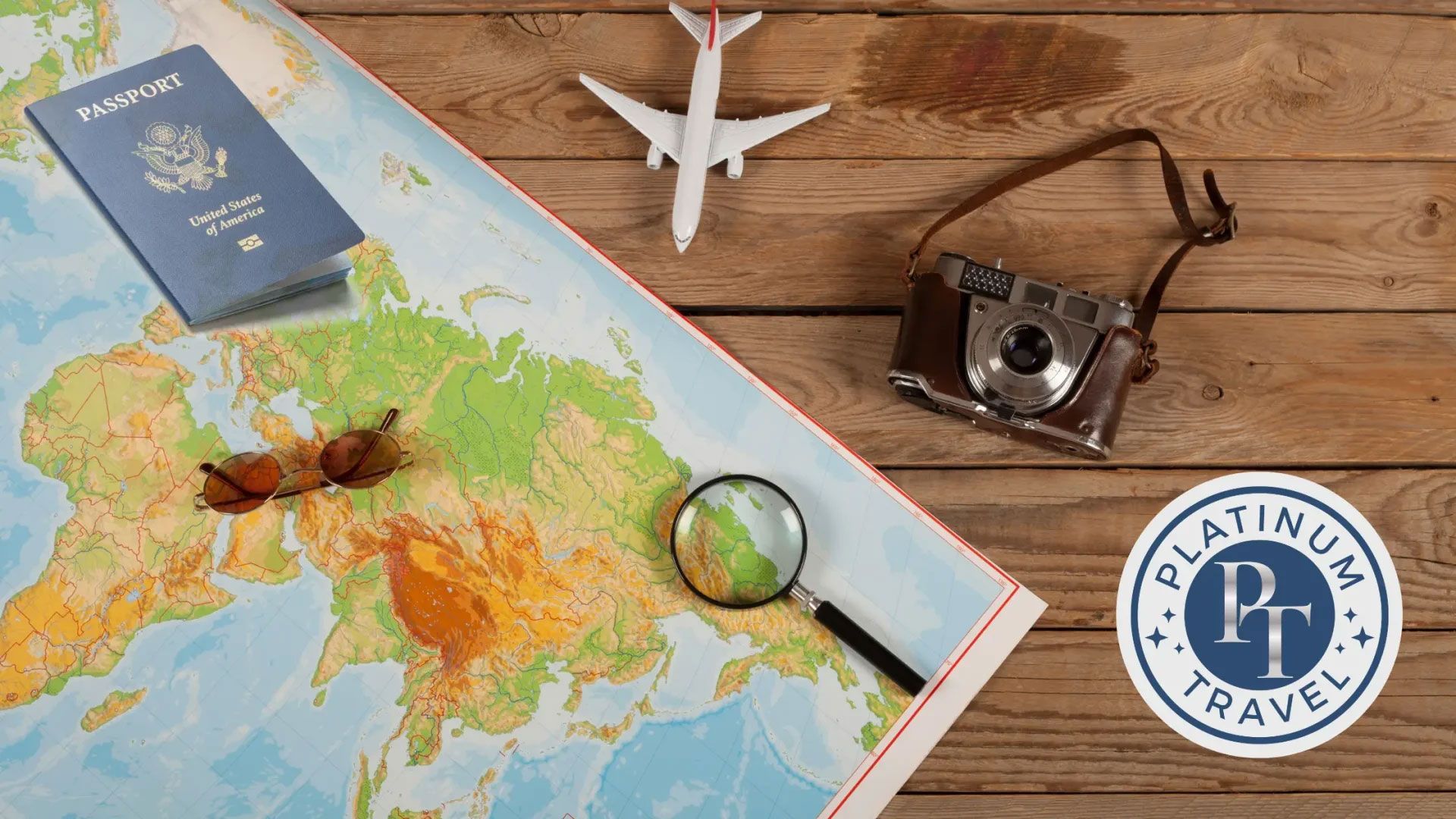 Travel planning flat lay with map, passport, toy plane, camera, glasses, and compass on a wooden table
