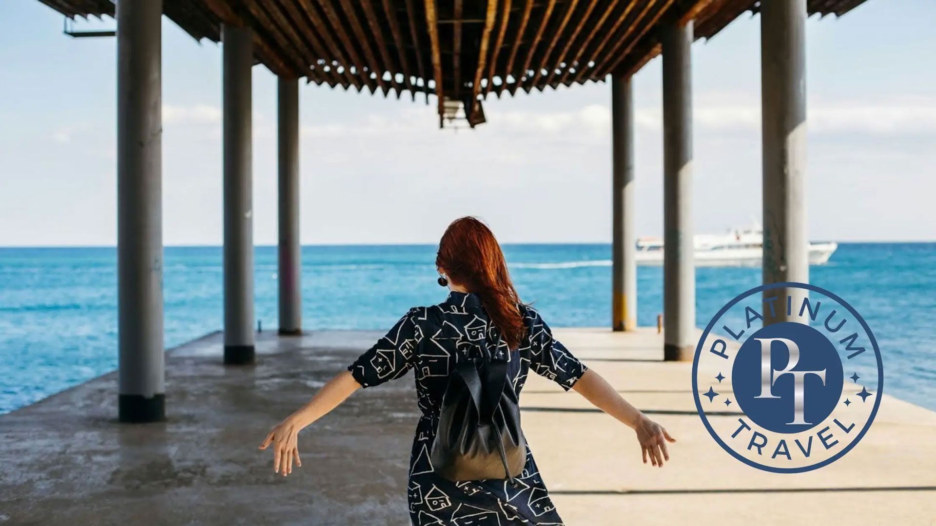 Woman in a black dress stands with arms outstretched on a seaside pavilion overlooking blue water. Woman in a black dress stands with arms outstretched on a seaside pavilion overlooking blue water.