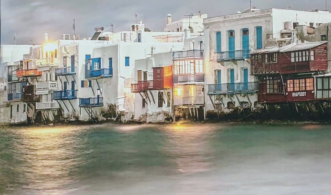 Colorful waterfront houses with balconies line a calm canal at dusk.