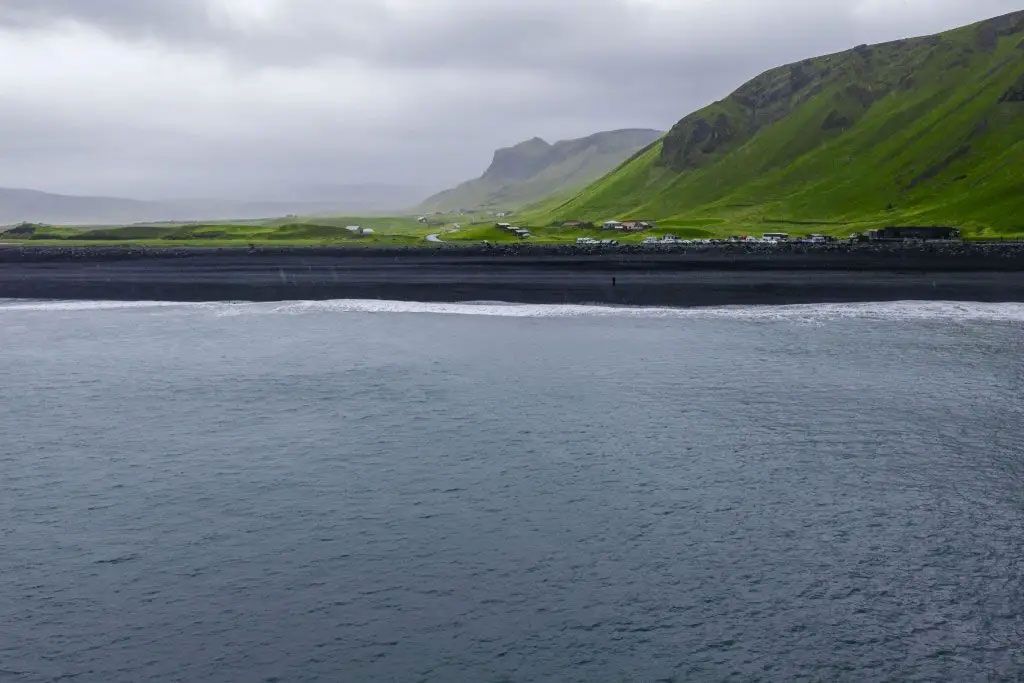 Calm gray sea beside a dark shoreline and green cliffs under cloudy skies Calm gray sea beside a dark shoreline and green cliffs under cloudy skies