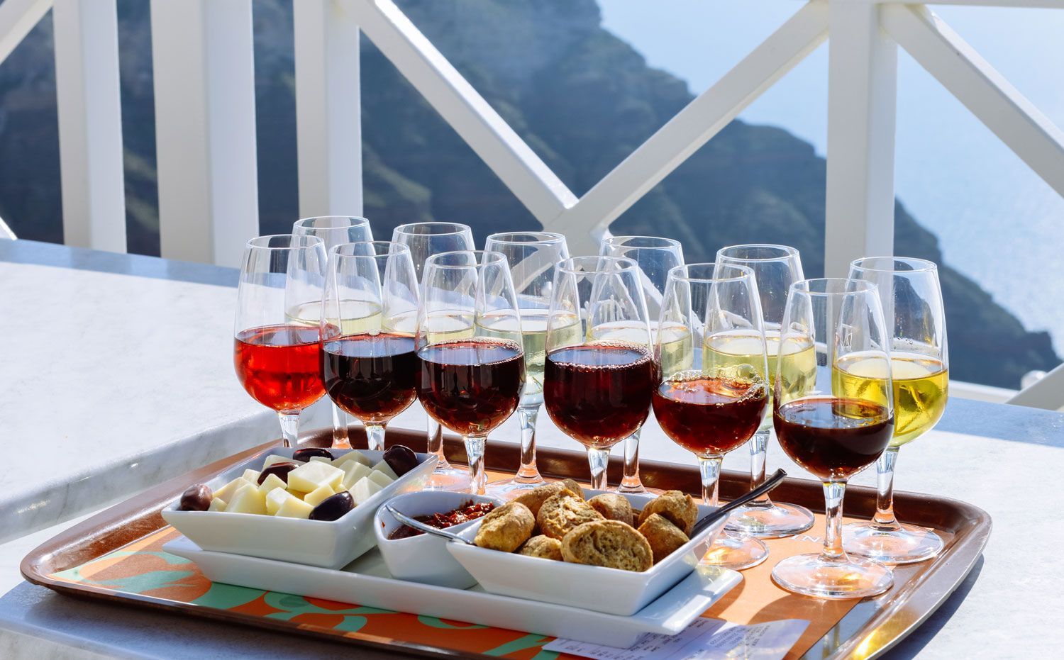 Wine glasses and appetizers on a sunlit balcony table overlooking the water