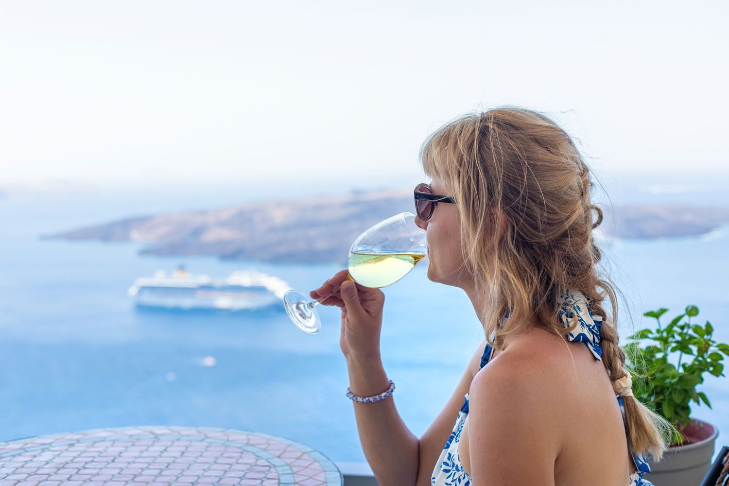 Woman sipping a drink while overlooking a blue sea and distant islands from a seaside terrace