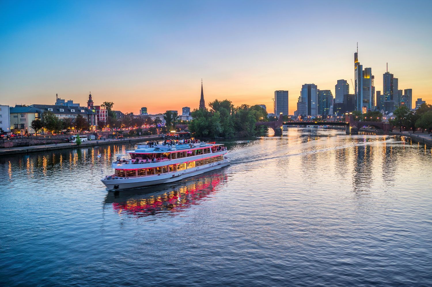 Boat on a river at sunset with a city skyline glowing in the background