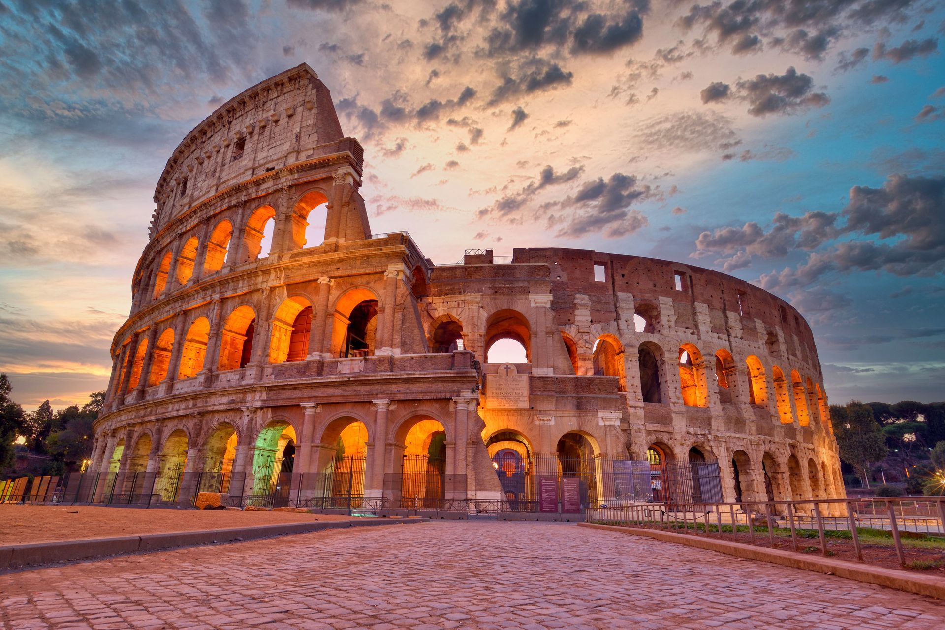 Colosseum in Rome at sunset with warm lights and a dramatic cloudy sky