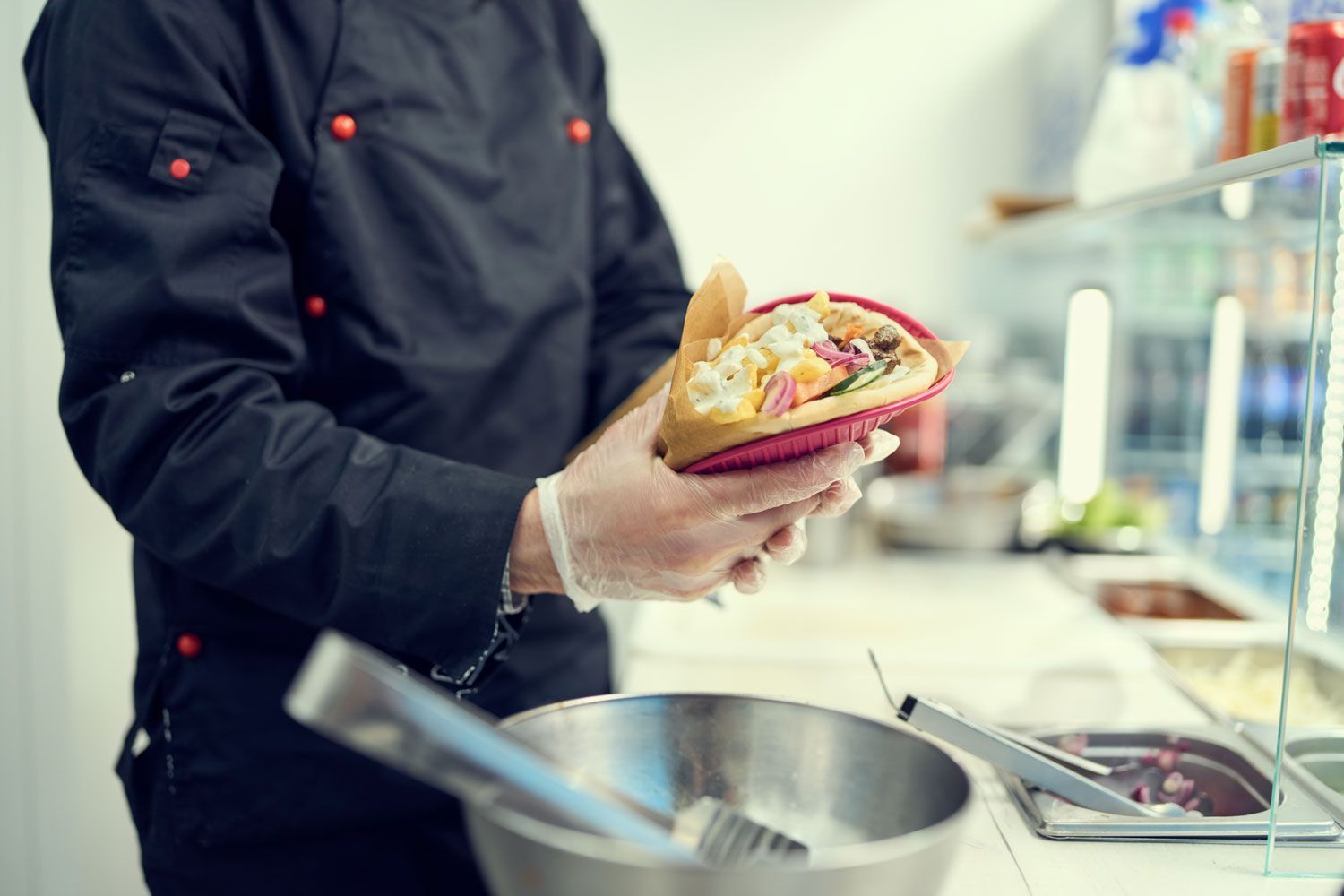 Chef holding a plated dish over a kitchen counter with a pot in the foreground