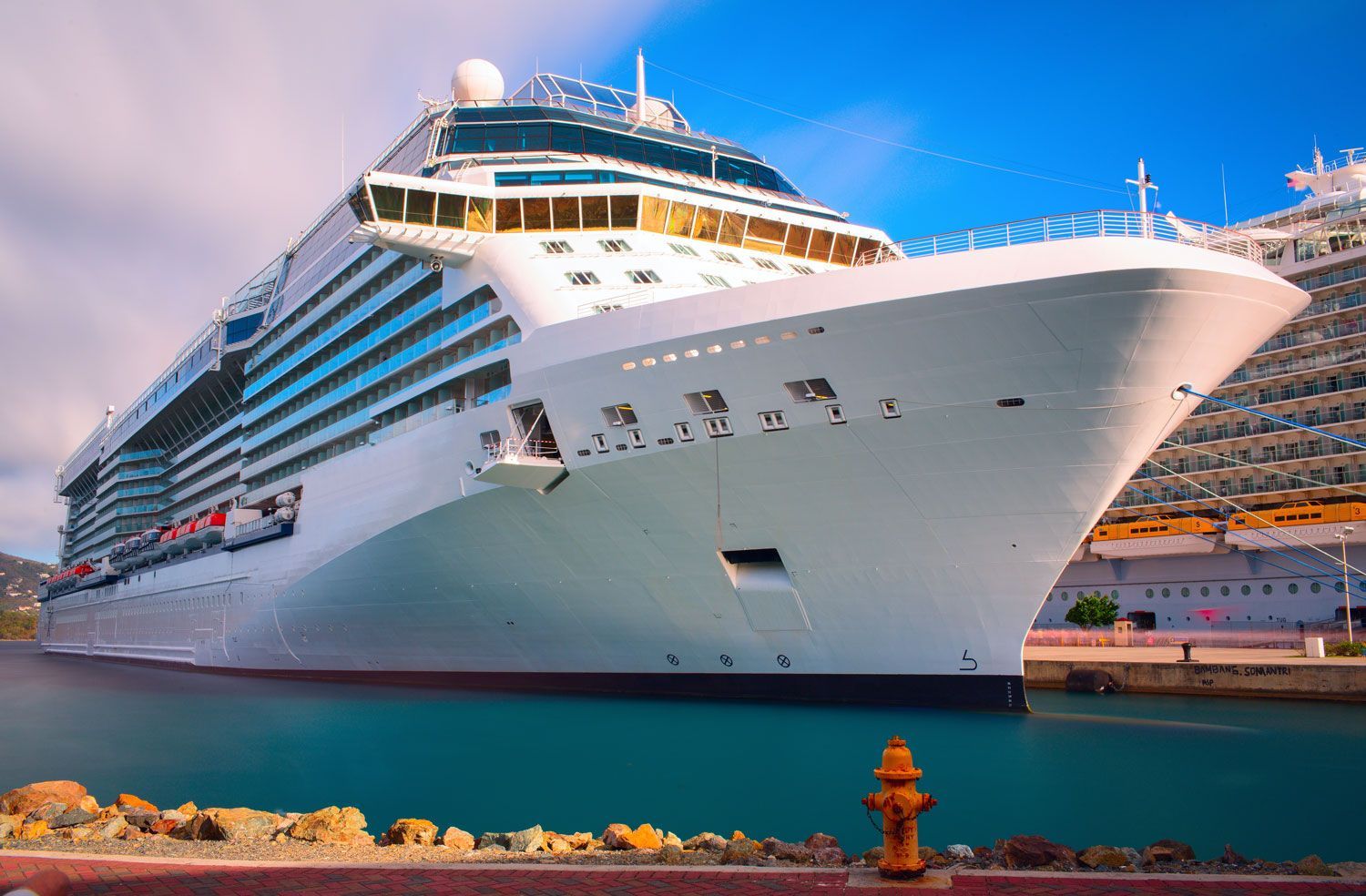 Large white cruise ship docked at a port under a pink sunset sky
