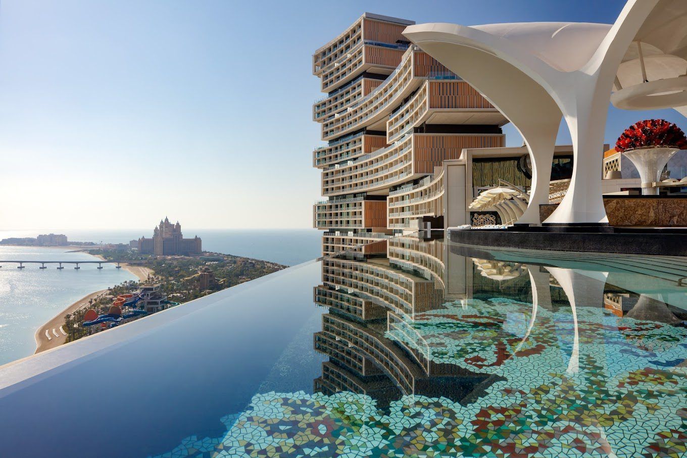Luxury seaside resort with an infinity pool, modern tower, and distant island skyline at sunset
