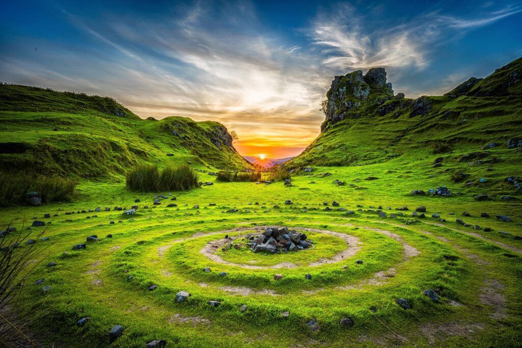 Sunset over a grassy spiral stone garden with green hills and a bright sky