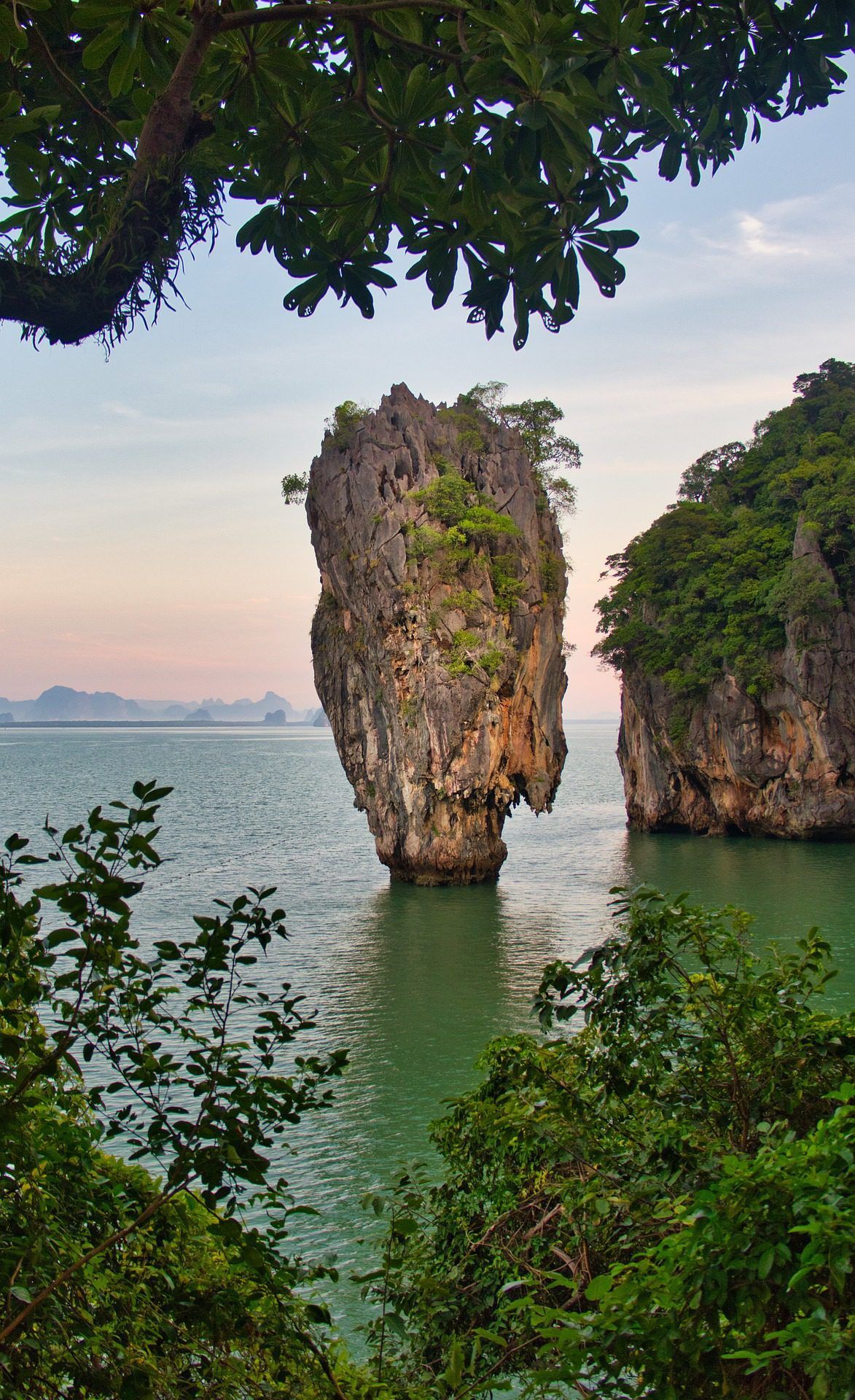 Rocky limestone islets rising from green water at sunset, framed by lush foliage.