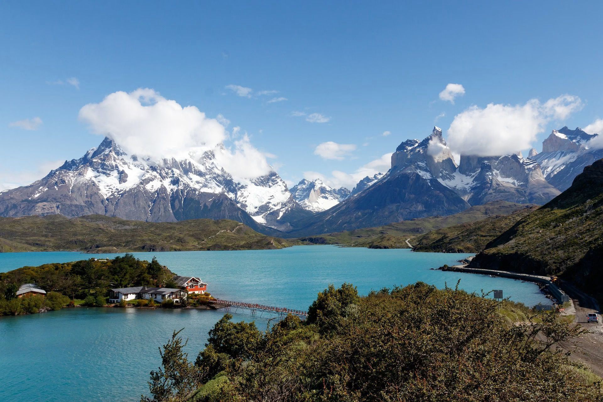 Snowy mountains above a turquoise lake with a small island and forested shore under a blue sky