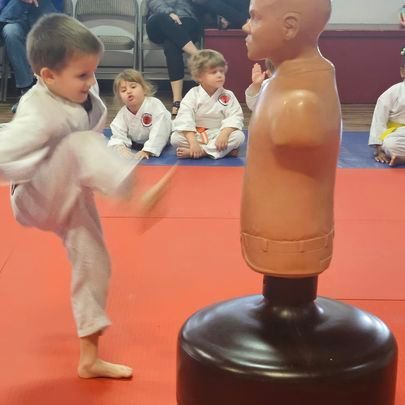 A young boy is kicking a mannequin in a martial arts class