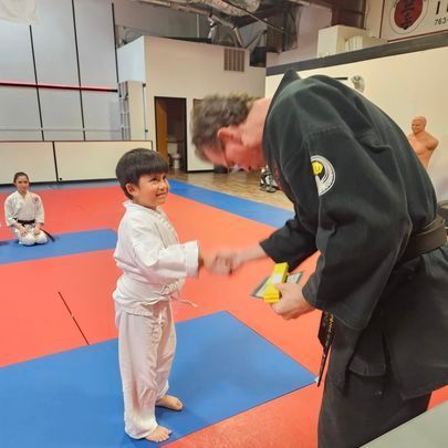 A man in a black karate uniform talks to a young boy
