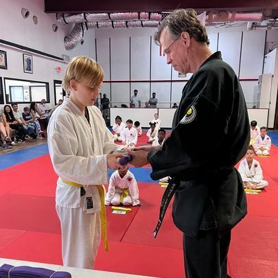 A man is giving a purple belt to a young boy