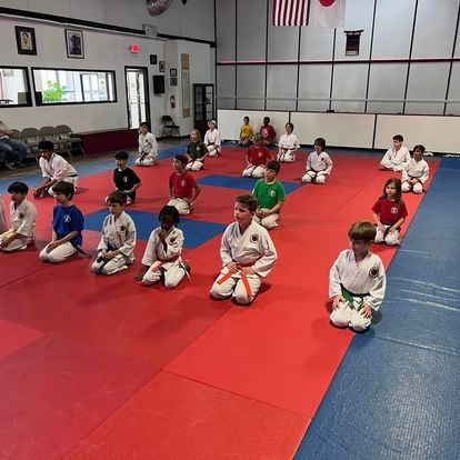 A group of children are sitting on a red and blue mat in a gym.