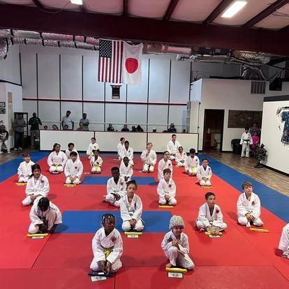 A group of children are sitting on a red and blue mat in a gym.