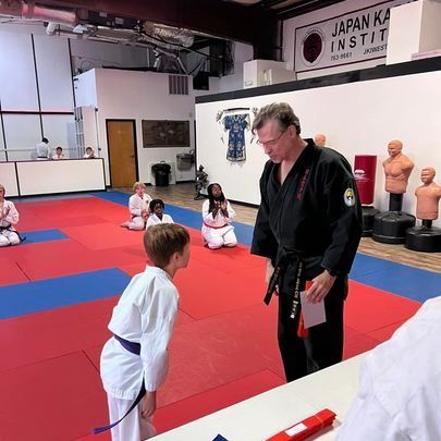 A man in a black karate uniform is talking to a boy in a karate class.