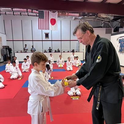 A man in a karate uniform is giving a yellow belt to a young boy.
