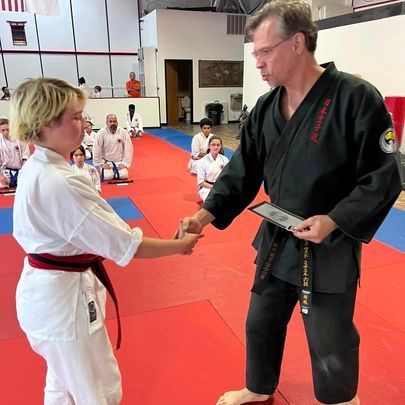 A man in a black karate uniform is shaking hands with a woman