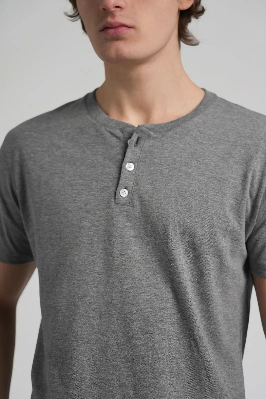 Camisa Henley gris de manga corta con tres botones sobre una persona, sobre un fondo liso.