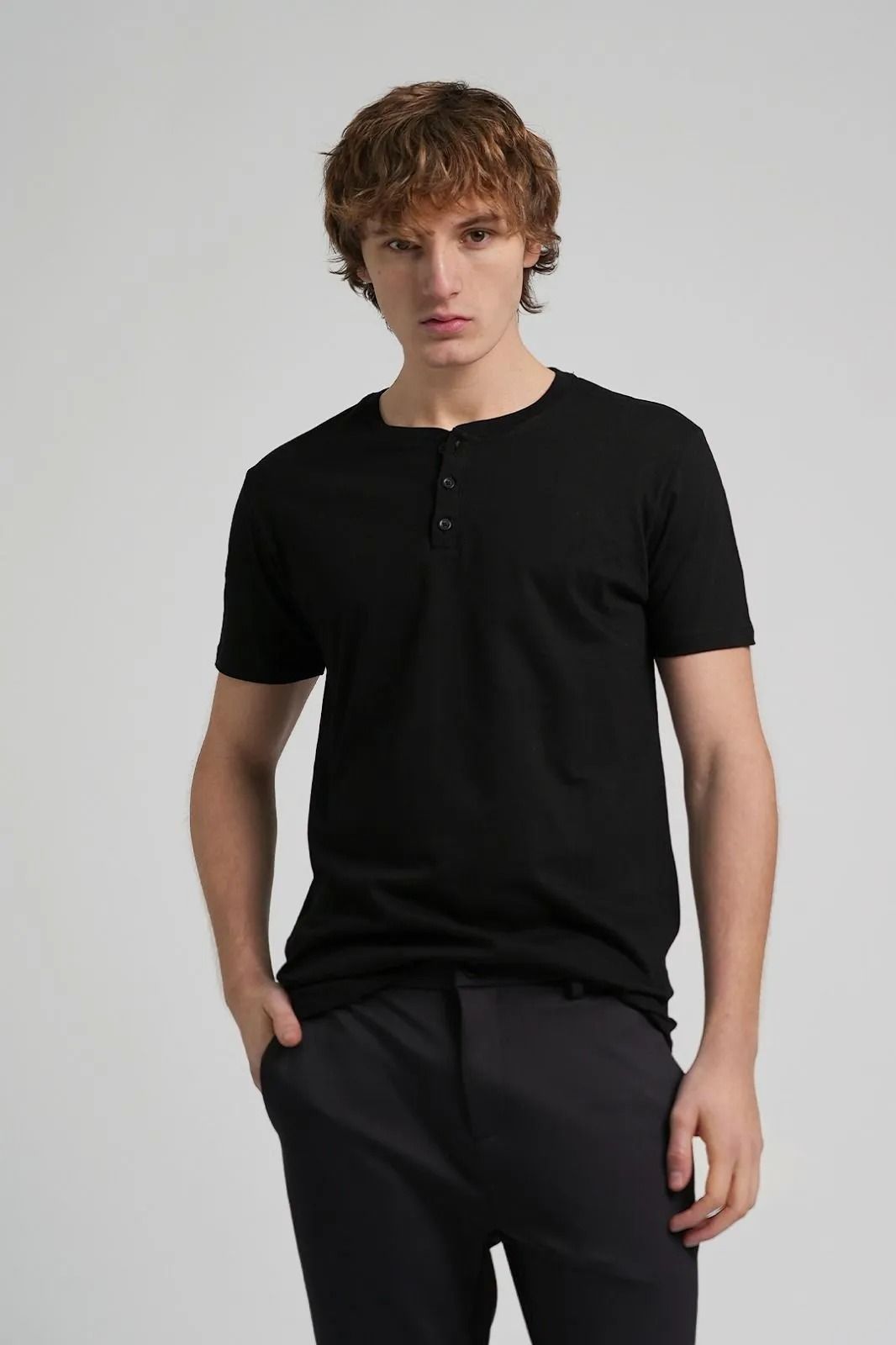 Persona vestida con camiseta y pantalón negros, de pie sobre un fondo gris claro.