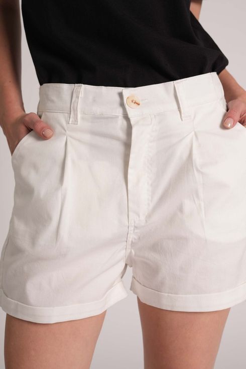 Una persona lleva unos pantalones cortos blancos de talle alto con las manos en los bolsillos, combinados con una camiseta negra.