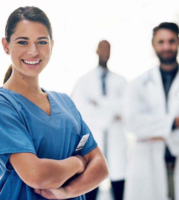 Smiling healthcare worker in blue scrubs with two doctors blurred in the background