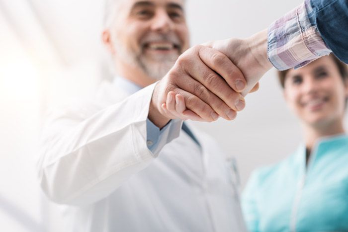 Doctor shaking hands with a patient in a bright clinic, with a nurse smiling in the background