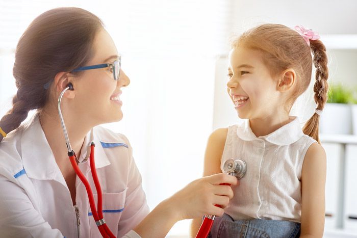 Doctor listening to a smiling child’s chest with a stethoscope in a bright clinic