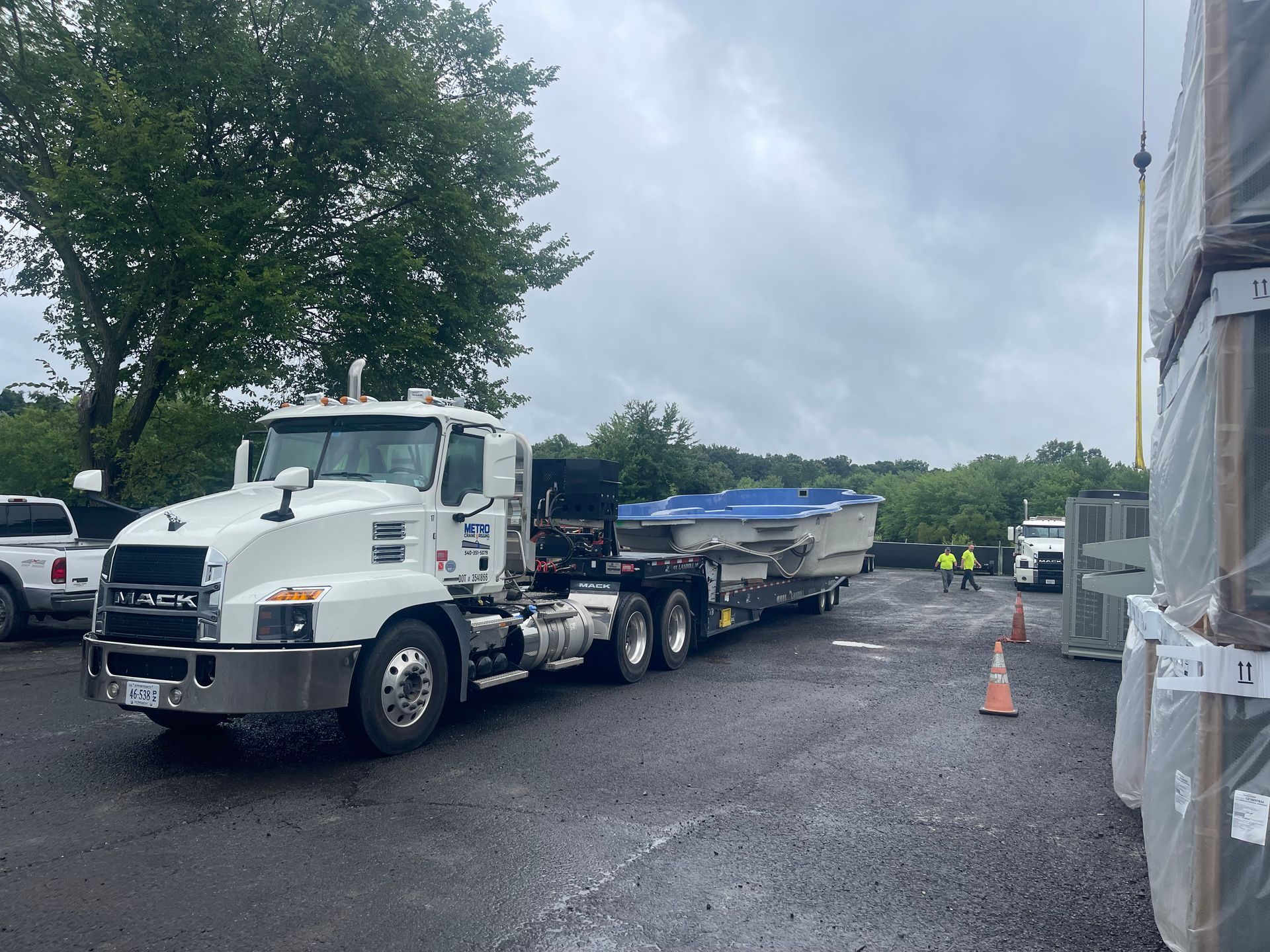 White semi-truck transporting a boat on a flatbed trailer on a paved lot.