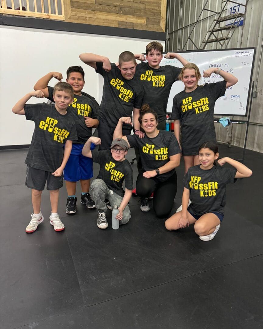 Group of kids and an adult flexing muscles in a gym, wearing