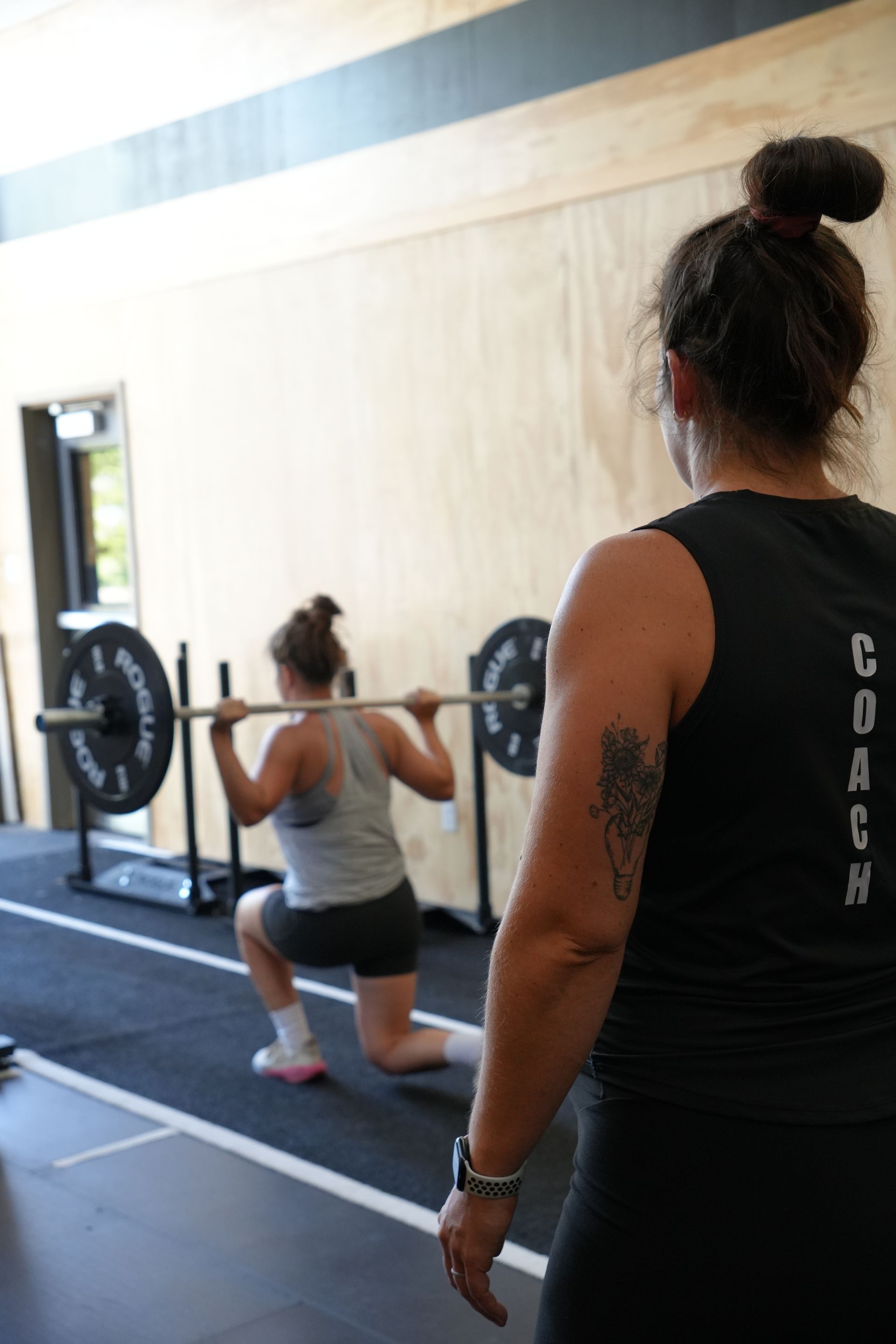 A man is talking to a woman in a gym while holding a barbell in a New Port, MN fitness class