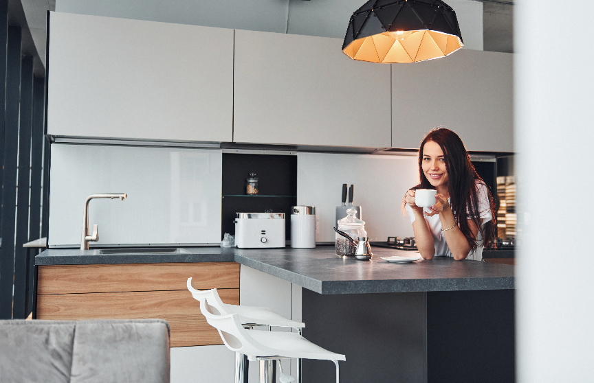 A woman is sitting at a kitchen counter drinking coffee.