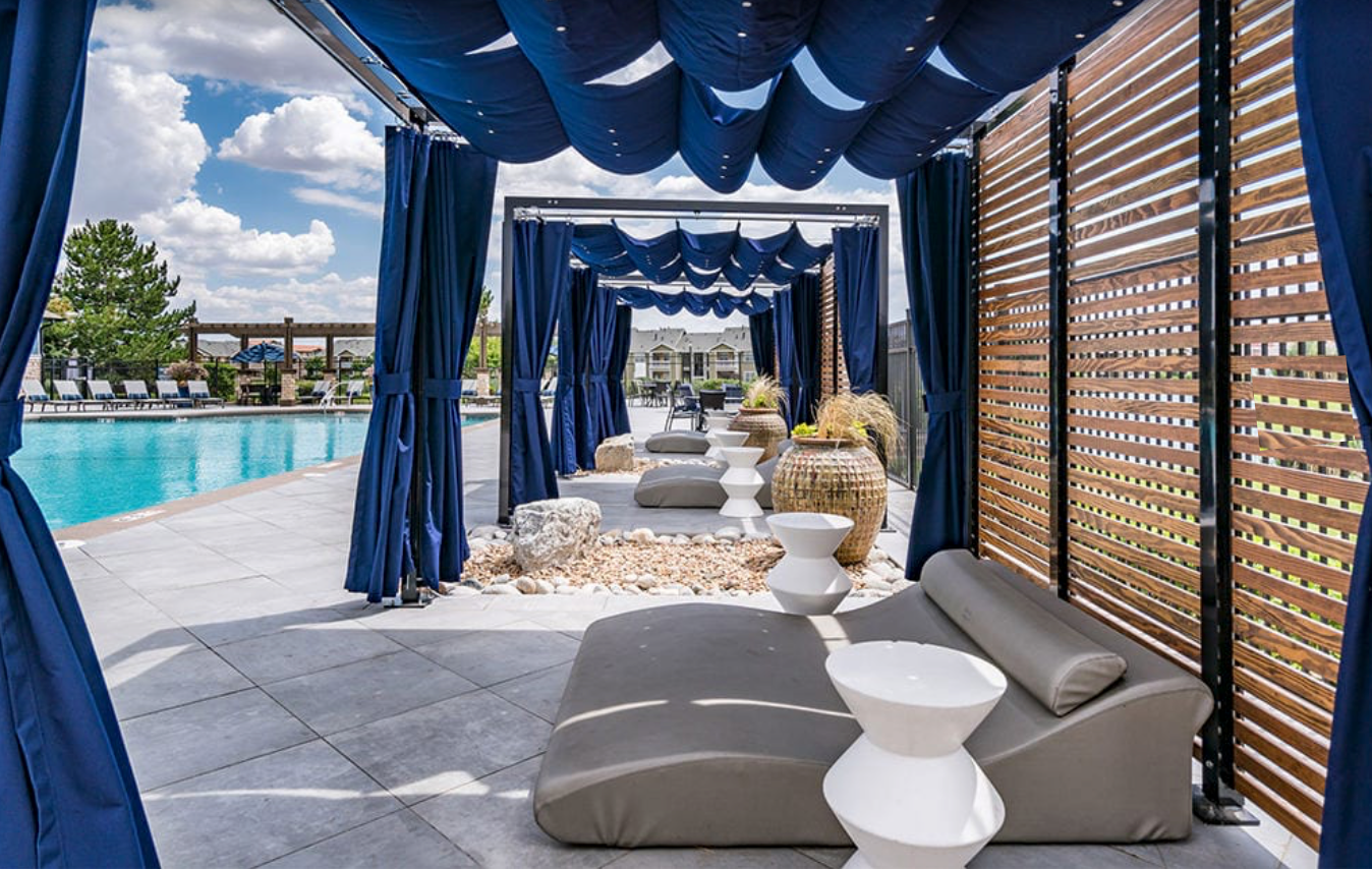 A row of lounge chairs under a canopy next to a swimming pool.