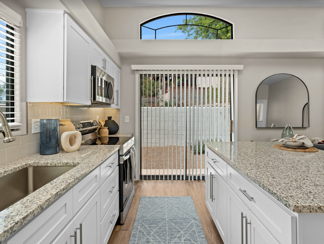 A kitchen with white cabinets , granite counter tops , stainless steel appliances and a sliding glass door.