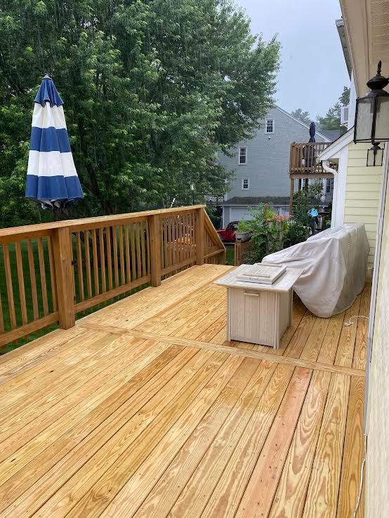 A wooden deck features a blue-and-white striped umbrella, a fire pit table, and covered furniture on a cloudy day.