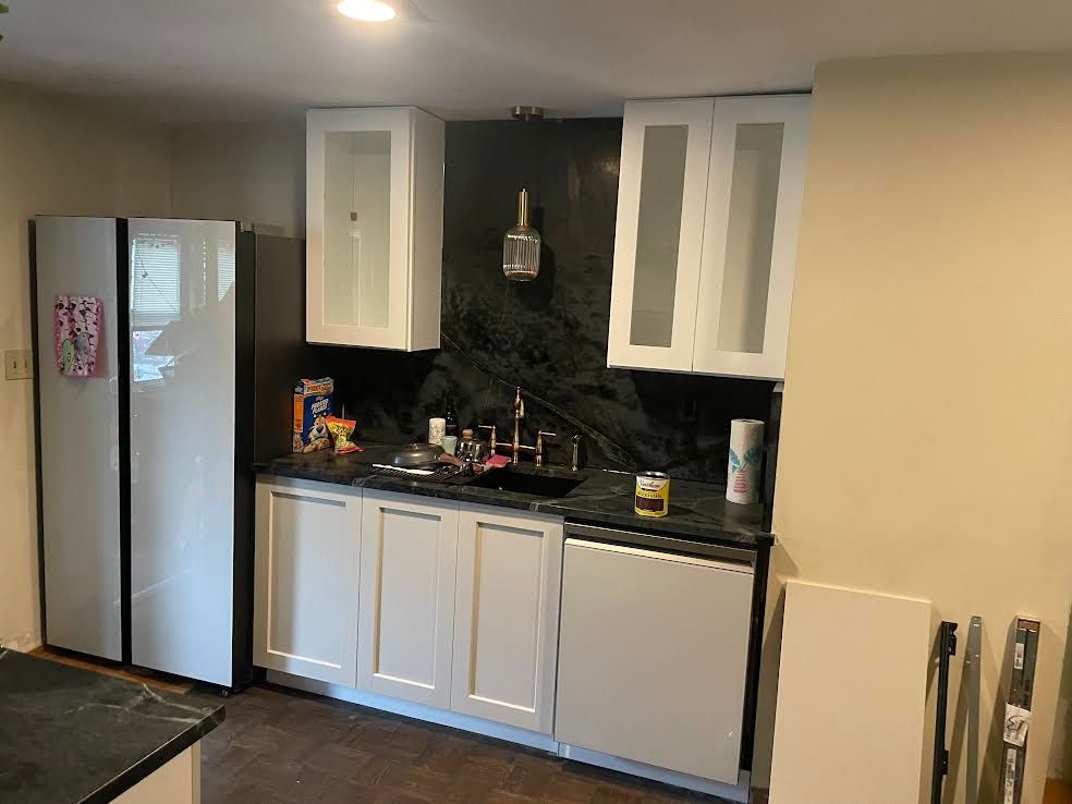 Kitchen area featuring white cabinets, a black tiled backsplash, a sink, and a modern side-by-side refrigerator.