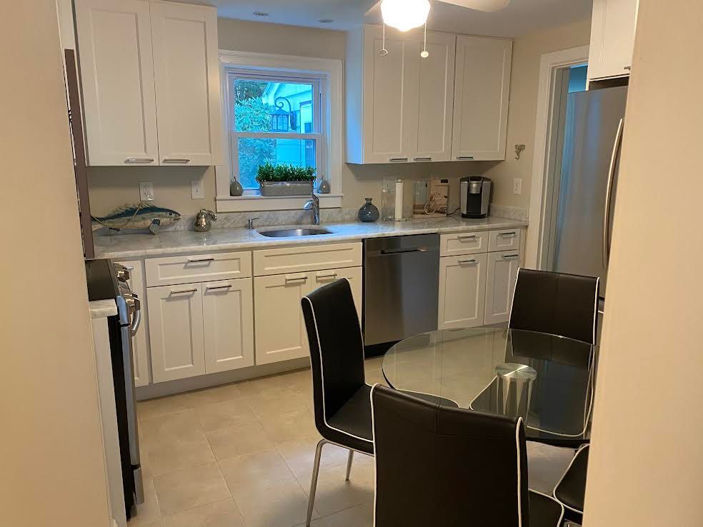 A bright kitchen with white cabinets, light countertops, stainless steel appliances, and a glass-top dining set.