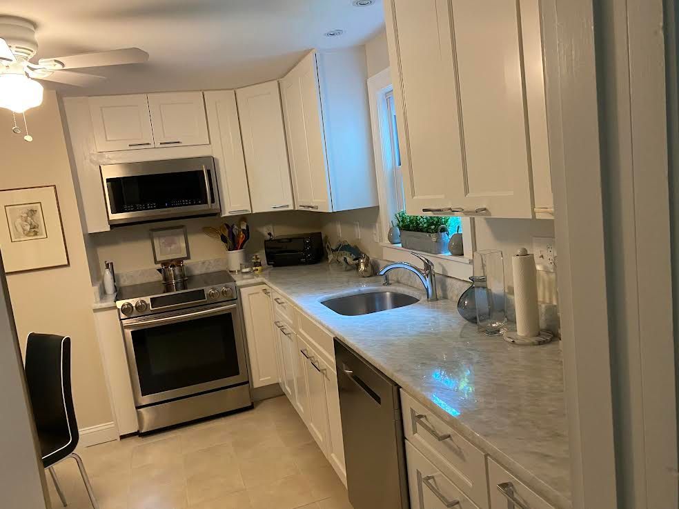 A clean, modern kitchen with white cabinets, stainless steel appliances, and a marble countertop.