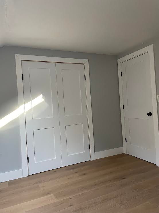 A corner of a room with gray walls, light wood floors, white double closet doors, and a standard white interior door.