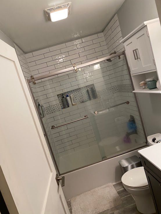 A bathroom with a tiled walk-in shower featuring a sliding glass door, a wall niche, a medicine cabinet, and a toilet.