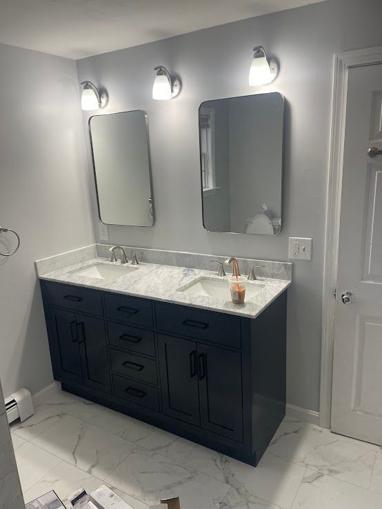 A modern bathroom with a dark blue double vanity, marble countertop, two rectangular mirrors, and bright wall lighting.