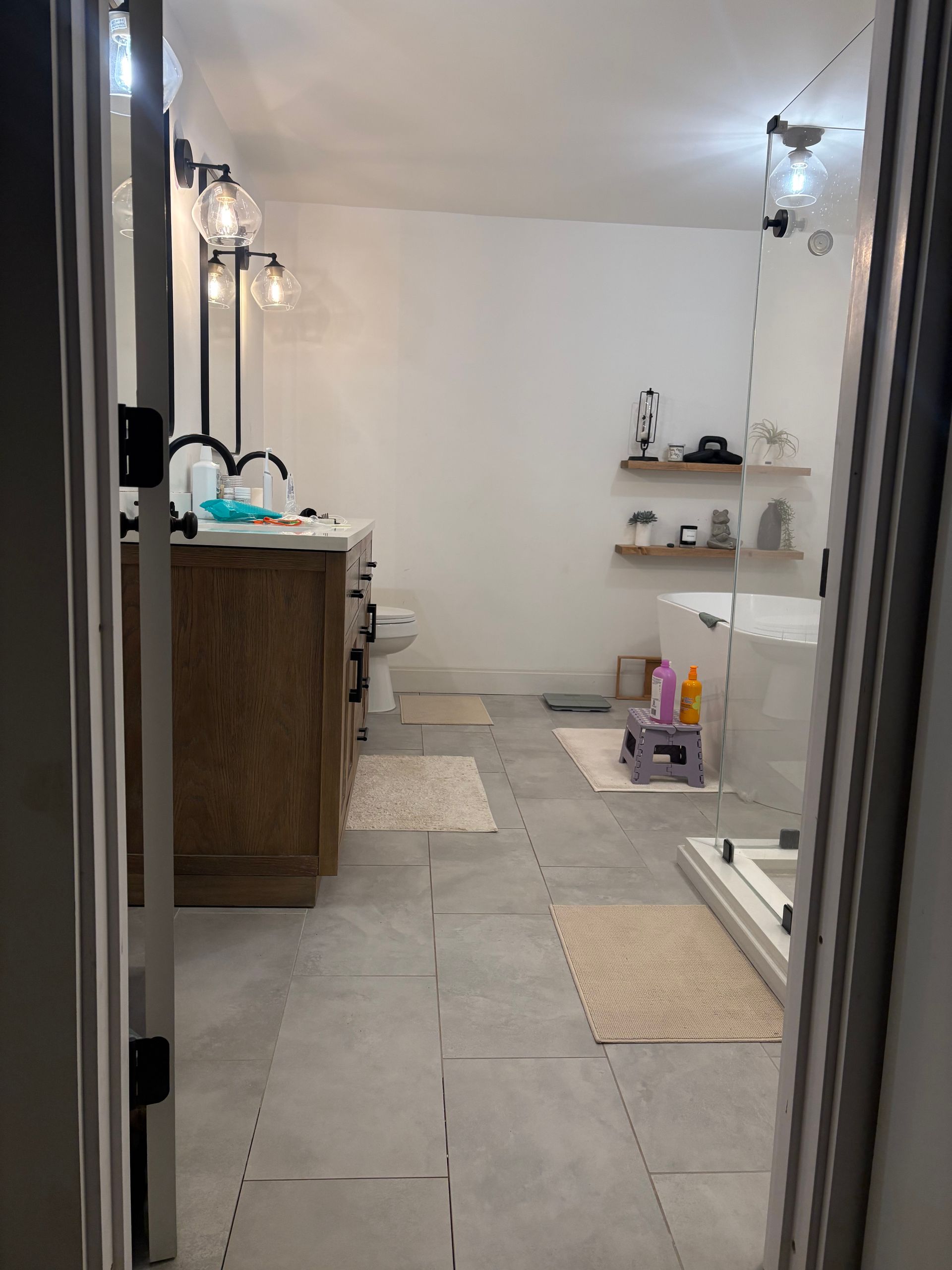 A bathroom featuring a wooden vanity, a walk-in shower, open shelves, and light gray tiled flooring.