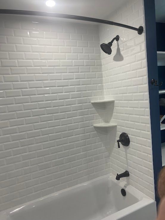 A bathtub and shower area with white subway tile walls, dark bronze fixtures, and two corner shelves.